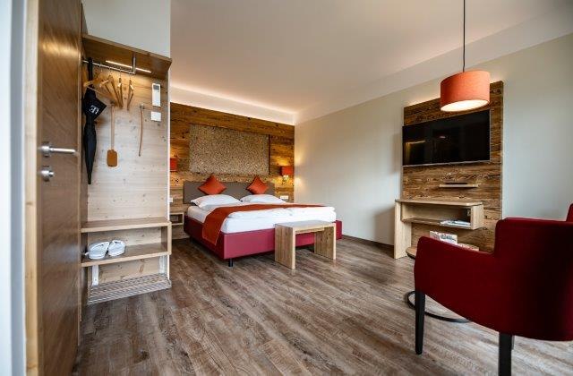 Modernes Hotelzimmer mit Doppelbett, Holzmöbeln und rotem Sessel.