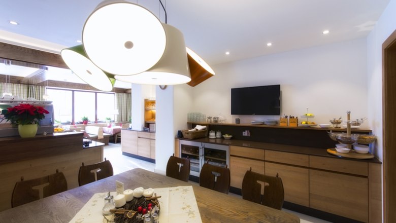 Ein modernes Restaurant mit Holzmöbeln, einem großen Tisch, dekorativen Lampen und einem Fernseher an der Wand.