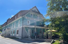 Traditionelles Gasthaus mit blauer Fassade und Terrasse bei sonnigem Wetter.