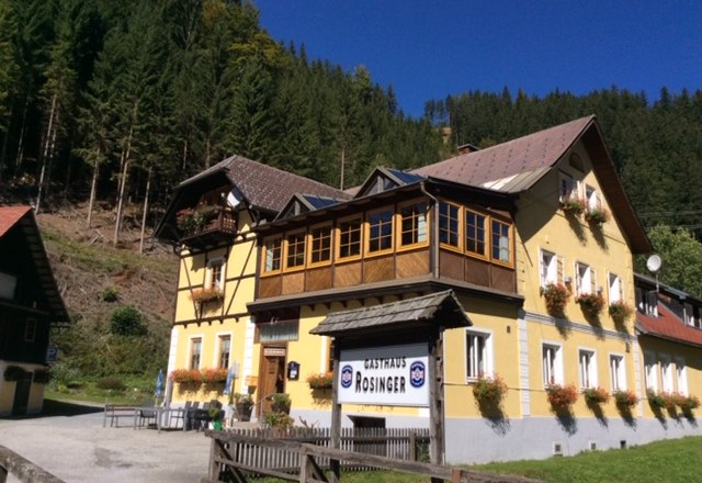 Ein gelbes Gasthaus mit Holzveranda und Blumenkästen, umgeben von Wald.
