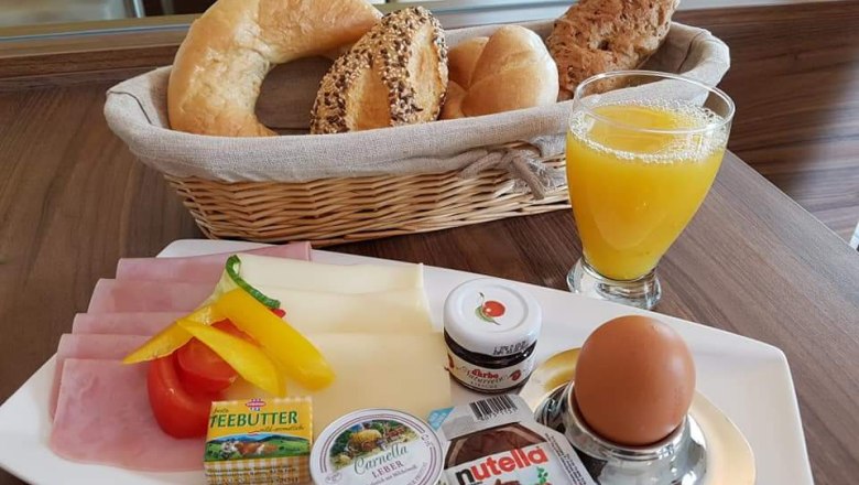 Frühstücksteller mit Brötchen, Aufschnitt, Ei und Orangensaft.