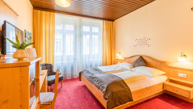Gem&uuml;tliches Hotelzimmer mit Doppelbett, Holzm&ouml;beln und rotem Teppich.