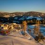 Luftaufnahme eines Gasthofs in verschneiter Berglandschaft bei Sonnenuntergang.