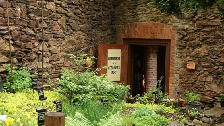 Eingang zu einem Laden in einem Steinhaus durch einem Garten mit Kräutern und Pflanzen.