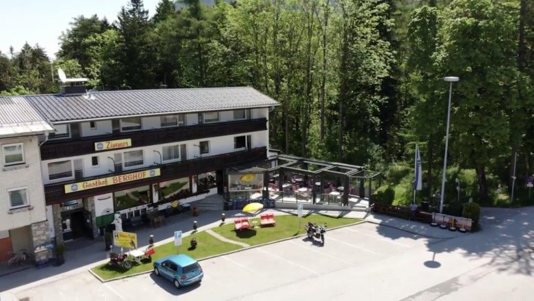 Au&szlig;enansicht des Gasthofs Berghof mit Terrasse und Parkplatz, umgeben von B&auml;umen.