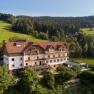 Hotel in l&auml;ndlicher Umgebung mit Wald und Wiesen im Hintergrund.