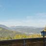 Blick von einem Restaurantbalkon auf eine bergige Landschaft mit Wald und einem schneebedeckten Gipfel im Hintergrund.