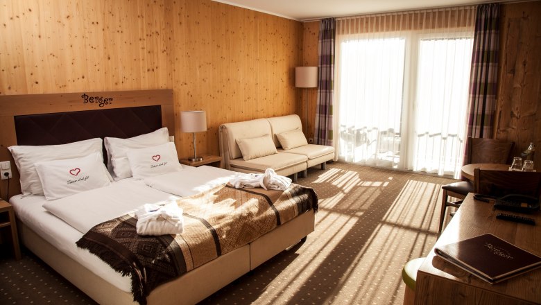 Hotelzimmer mit Doppelbett, Sofa und Holzmöbeln, sonnendurchflutet durch das große Fenster.