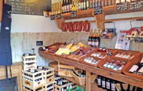 Innenansicht eines Hofladens mit Regalen voller regionaler Produkte wie Wein, Wurst, Gew&uuml;rze und &Ouml;l.