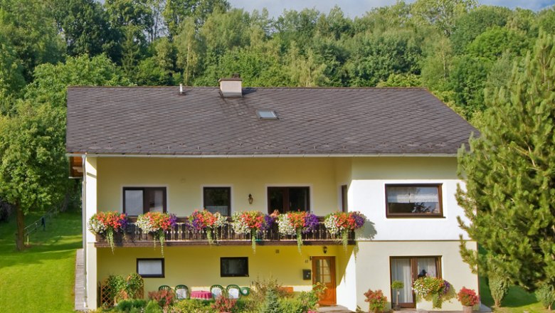 A mi házunk, © Wachabauer Kétemeletes sárga ház erkéllyel és virágokkal, fákkal és kerttel körülvéve.