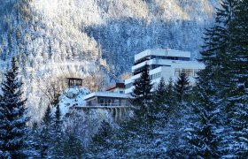 Winterliche Ansicht des Sporthotels Semmering umgeben von schneebedeckten B&auml;umen und Bergen.