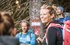 Gruppe von Wanderern vor einem Baumstamm mit Markierung.