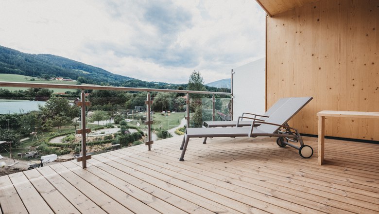 Holzterrasse mit Liegestuhl und Blick auf grüne Landschaft und Berge.