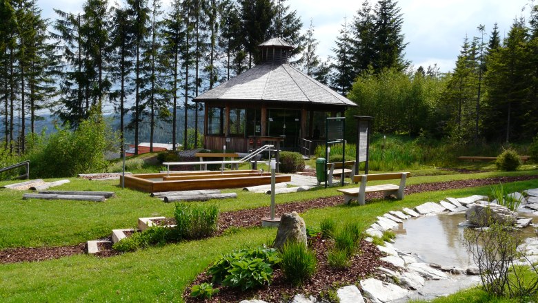 Ein kleiner Pavillon in einem grünen Park mit Bäumen und einem Teich.