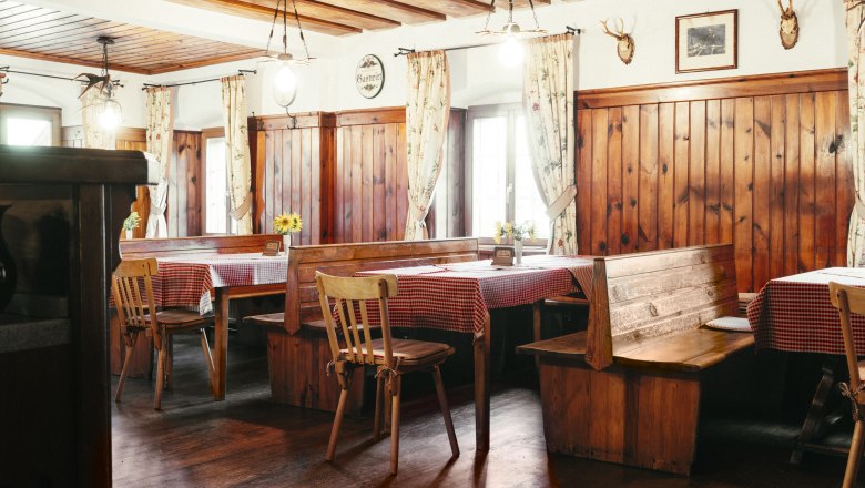 Gemütliche Gaststube mit Holzmöbeln und karierten Tischdecken.