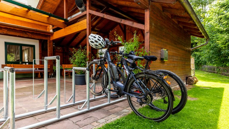 Fahrr&auml;der in einem Fahrradst&auml;nder vor einem Holzgeb&auml;ude mit Terrasse.