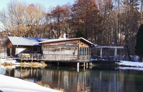 Ein Restaurant am Ufer eines Teiches im Winter, umgeben von B&auml;umen.