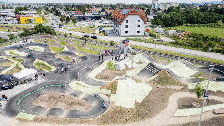 Luftaufnahme einer Pumptrack-Anlage in Wiener Neustadt mit Radfahrern und umliegender Stadtlandschaft.
