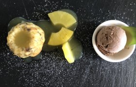 Dessert mit Kuchen, Ananas und Schokoladeneis auf schwarzem Teller.