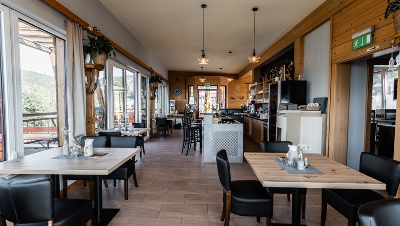 Innenansicht eines modernen Caf&eacute;s mit Holzm&ouml;beln und gro&szlig;en Fenstern.