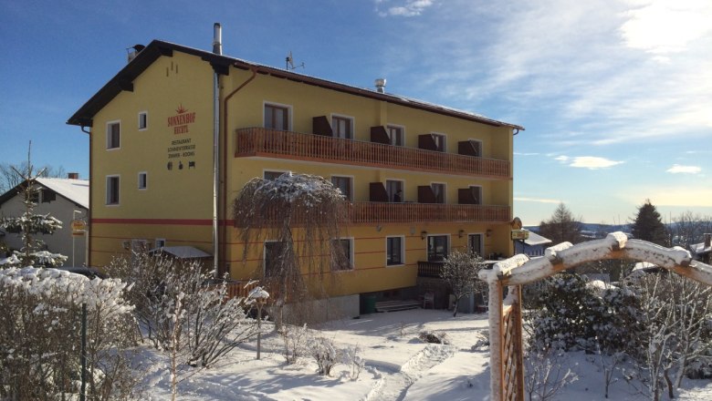 Sonnenhof, Winter, © Johannes Hechtl Gelbes Gebäude namens Sonnenhof im Winter mit Schnee bedeckt, blauer Himmel im Hintergrund.
