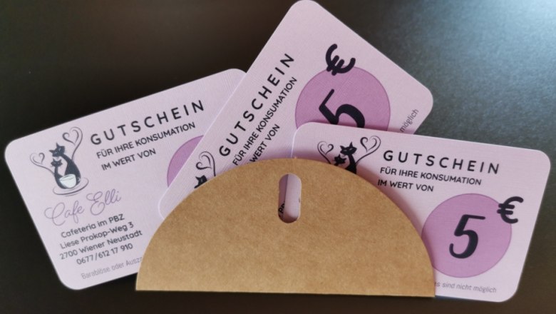 Drei rosafarbene Gutscheine im Wert von 5 Euro f&uuml;r das Cafe Elli, teils in einem Umschlag.