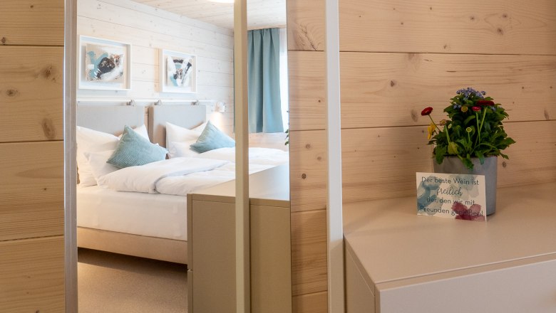 Ein gem&uuml;tliches Schlafzimmer mit Holzw&auml;nden, einem Bett mit blauen Kissen und einem kleinen Tisch mit einer Pflanze und einer Karte.