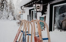Verschneite Hütte mit Schlitten davor.