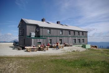 Holzgebäude in den Bergen mit Menschen auf Bänken davor.