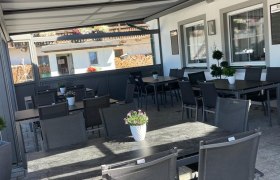 &Uuml;berdachte Terrasse mit Tischen und St&uuml;hlen, dekoriert mit Blumen.