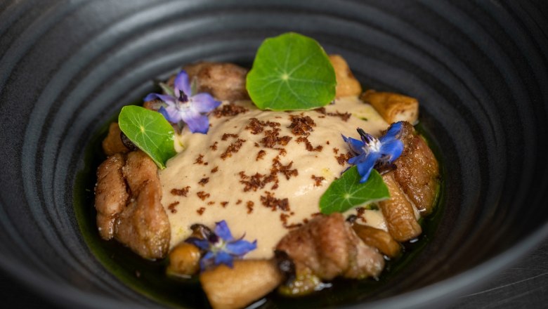 Ein elegantes Gericht in einer schwarzen Schale, dekoriert mit essbaren Bl&uuml;ten und gr&uuml;nen Bl&auml;ttern.
