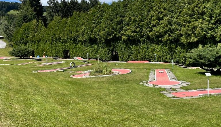 Minigolfanlage mit grüner Wiese und Bäumen im Hintergrund.