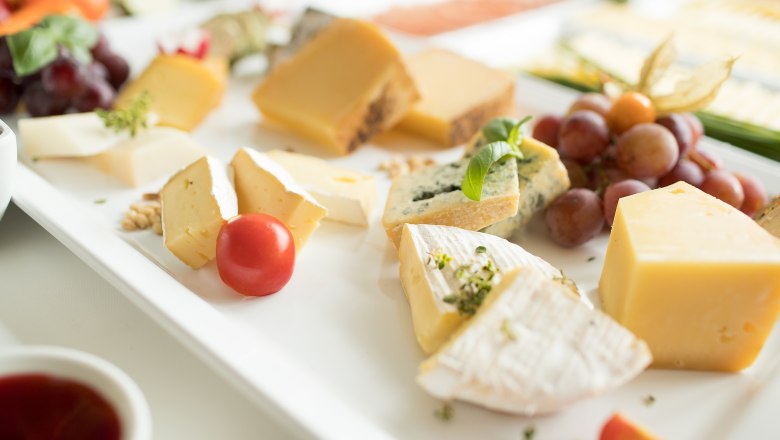 Verschiedene Käsesorten auf einem weißen Teller, dekoriert mit Trauben und einer Kirschtomate.