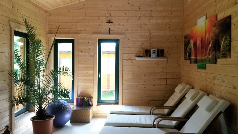 Innenraum einer Sauna mit Holzverkleidung, Liegest&uuml;hlen, einer Palme und einem Bild an der Wand.