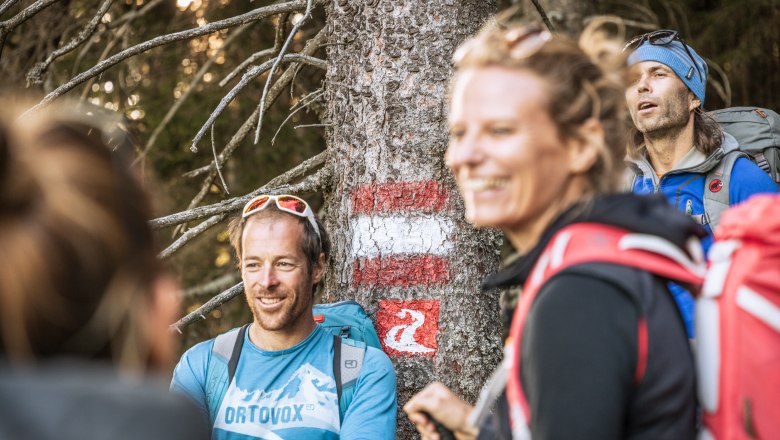 Gruppe von Wanderern vor einem Baumstamm mit Markierung.