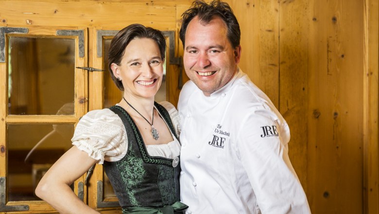 Ein Mann in Kochjacke und eine Frau in traditioneller Tracht lächeln in die Kamera.