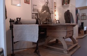 Ausstellung mit alten Haushaltsger&auml;ten und einem Portr&auml;t im Hintergrund.