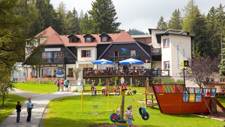 Ein Gasthof in den Alpen mit Spielplatz und Menschen im Freien.