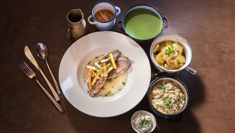 Tafelspitz in einem weißen Teller. Klassische Beilagen in kleinen Schälchen rund um den Teller gruppiert.