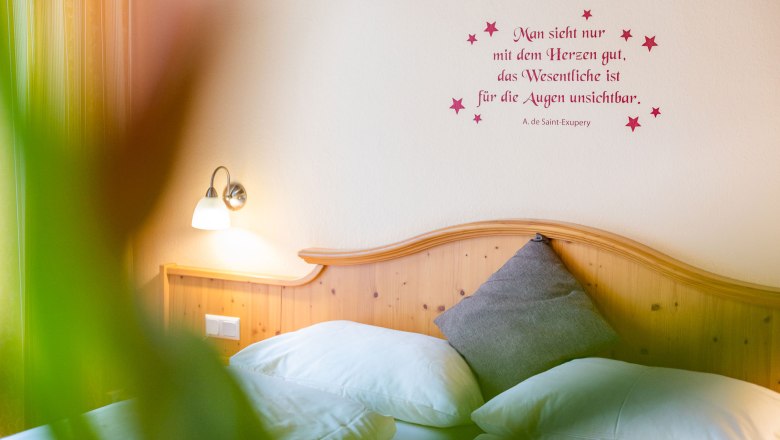 Gem&uuml;tliches Schlafzimmer mit Zitat an der Wand und Holzkopfteil.