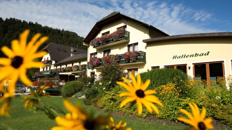 Helles Geb&auml;ude mit Holzbalkone und zahlreichen Blumenk&auml;sten.