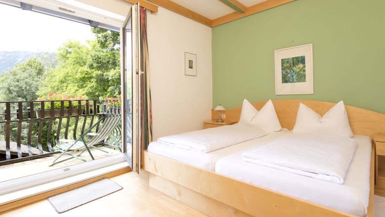 Helles Zimmer mit Doppelbett, grün gestrichener Wand und Balkon mit Bergblick.