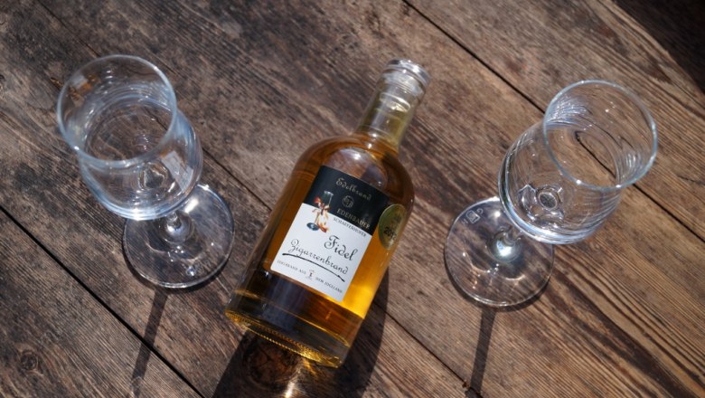 Eine Flasche Edelbrand mit zwei Gl&auml;sern auf einem Holztisch.