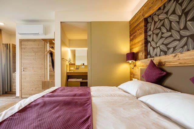 Modern eingerichtetes Hotelzimmer mit Doppelbett, Holzwänden und Blick ins Badezimmer.