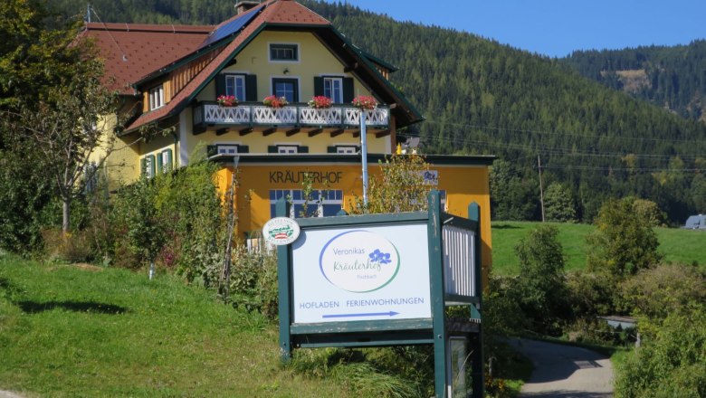 Ein gelbes Geb&auml;ude mit der Aufschrift 'Kr&auml;uterhof' und einem Schild 'Veronikas Kr&auml;uterhof' in l&auml;ndlicher Umgebung.