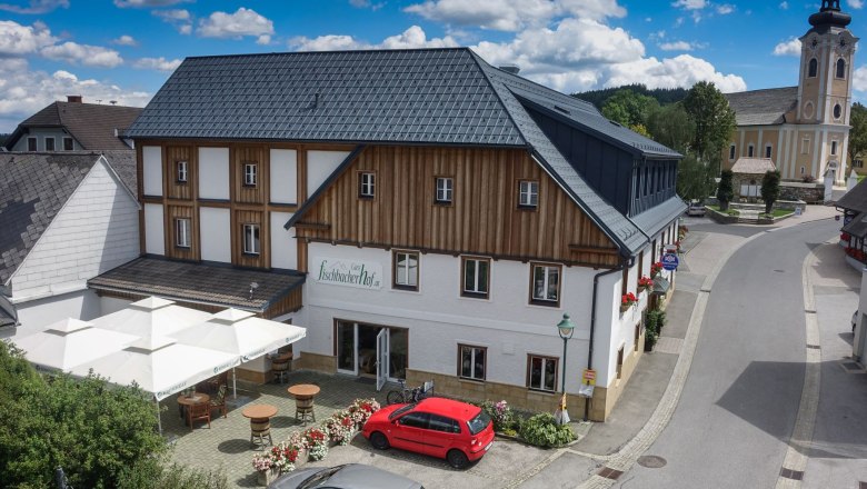 Luftaufnahme eines Gasthauses mit Terrasse, daneben eine Kirche.