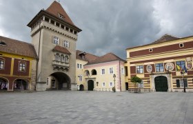 Historischer Platz mit alten Geb&auml;uden und einem Turm unter bew&ouml;lktem Himmel.