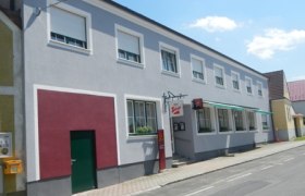 Zweistöckiges Gebäude mit grauer Fassade und mehreren Fenstern an einer Straße.