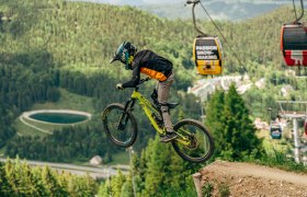 Mountainbiker springt im Bikepark Semmering, im Hintergrund Seilbahn und Wald.