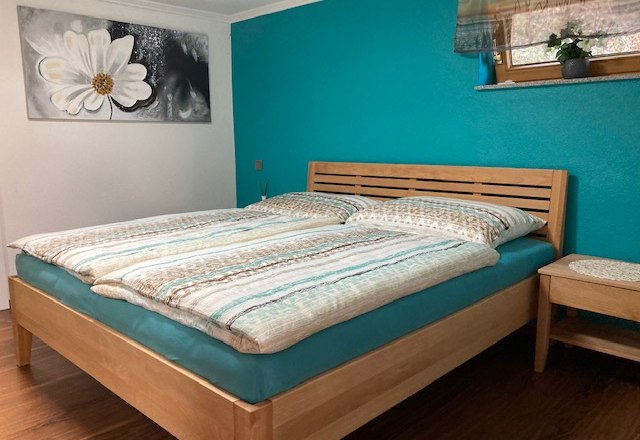 Schlafzimmer mit Doppelbett, t&uuml;rkisfarbener Wand und Blumenbild.